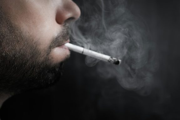 A close-up of a man's profile, smoking a cigarette with visible smoke.