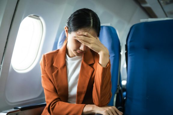 A woman in a plane seat appears stressed, face covered by her hand.